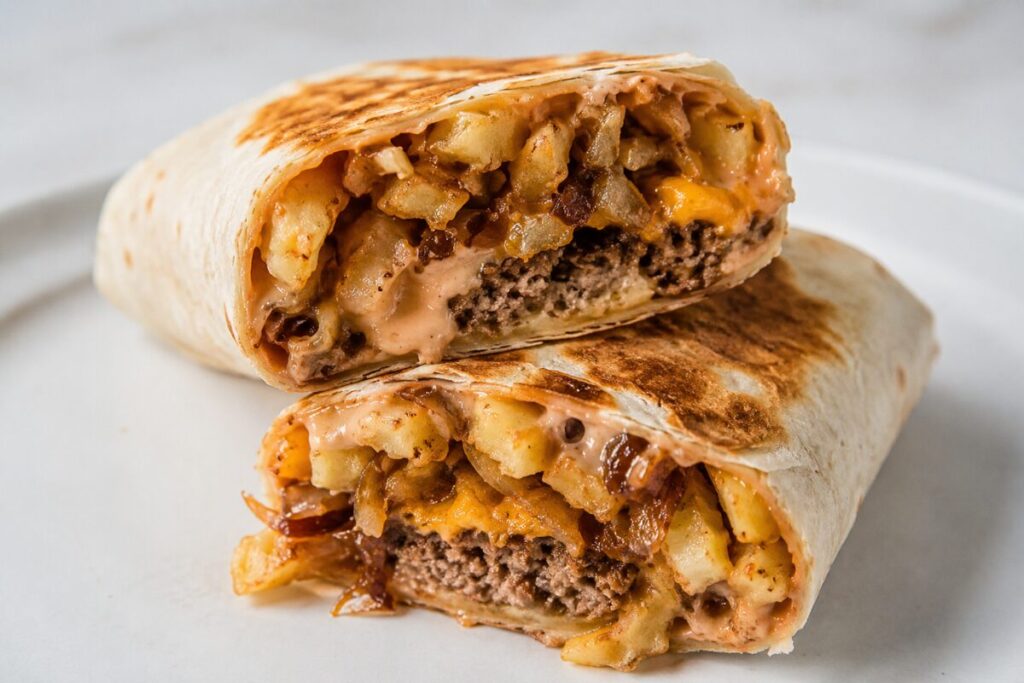 A stuffed tortilla cut in half showing crinkle fries, a burger patty, and melted cheese with sauce.