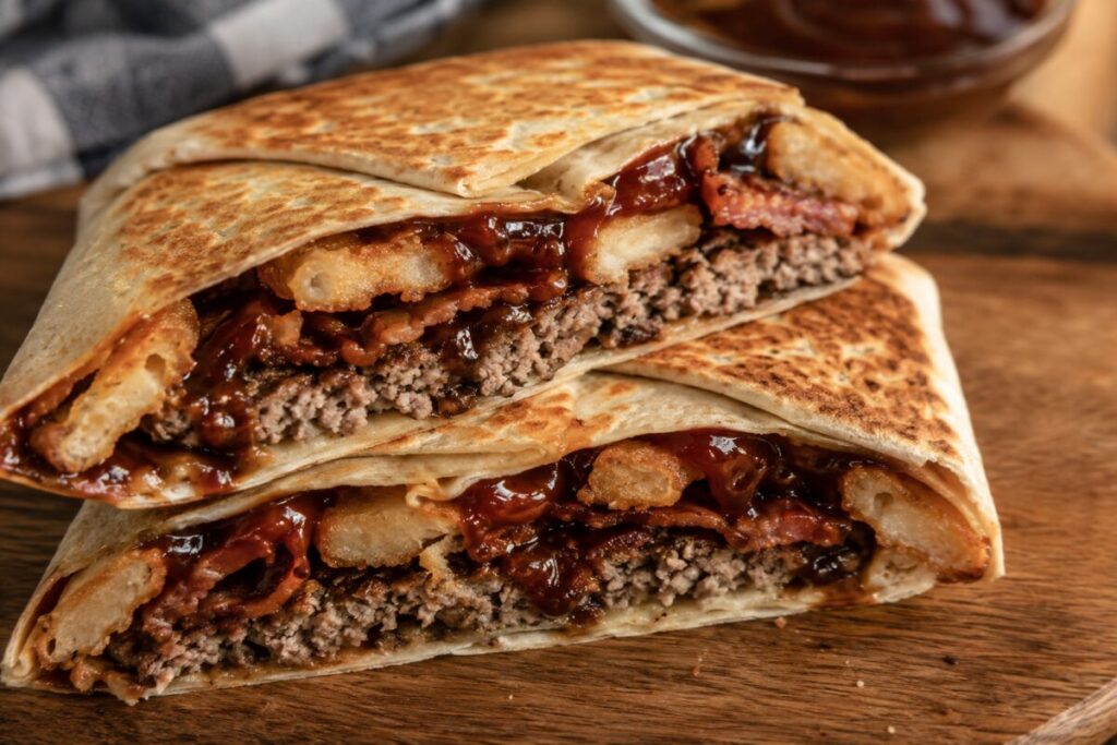 A sliced hexagonal wrap oozing with barbecue sauce, bacon, and a burger patty.