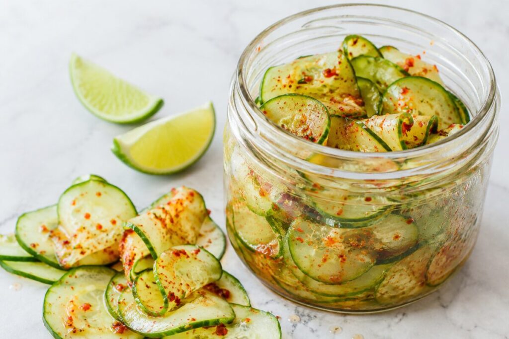 Thin cucumber slices and ribbons with chili-lime seasoning inside a clear glass jar.