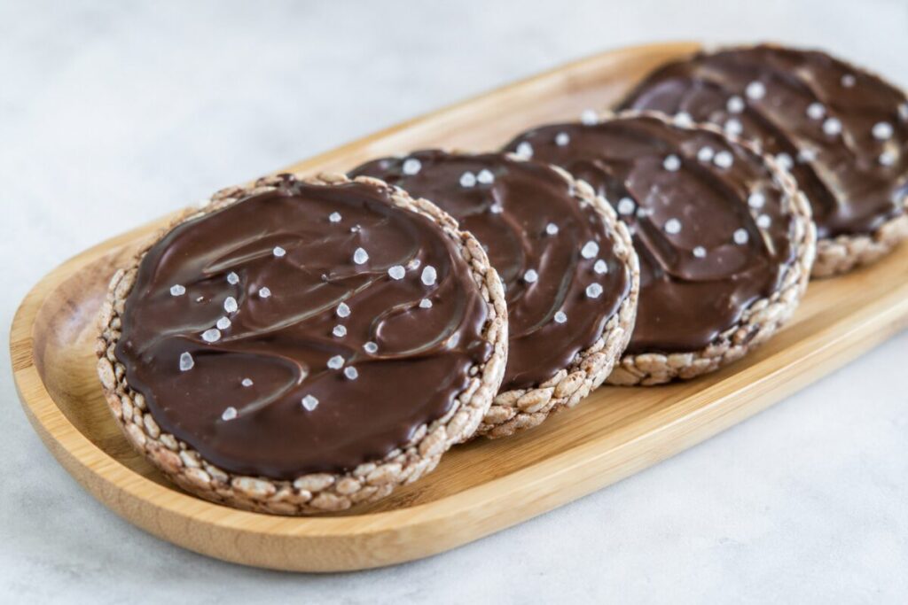 Rice cakes topped with dark chocolate and coarse sea salt on a bamboo tray.