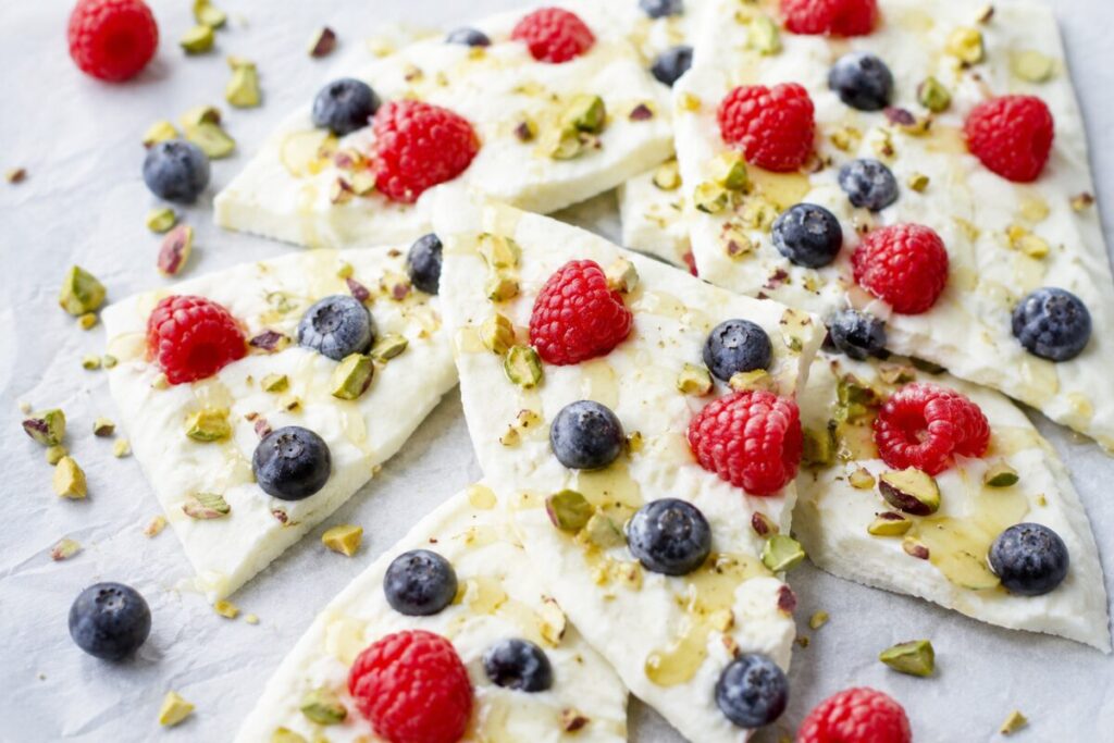 Broken pieces of frozen Greek yogurt bark topped with berries, pistachios, and honey drizzle.