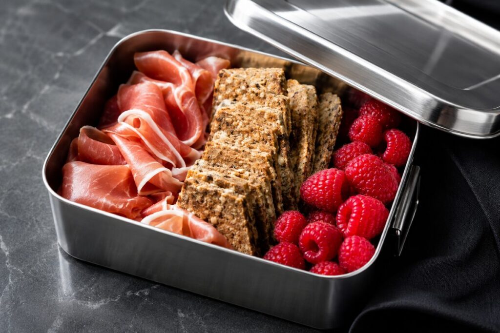 Stainless steel lunchbox packed with charcuterie style meats, cheeses, and berries.