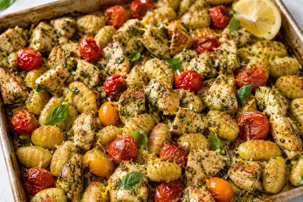 A sheet pan dinner featuring pesto-coated chicken, roasted tomatoes, and crispy gnocchi.