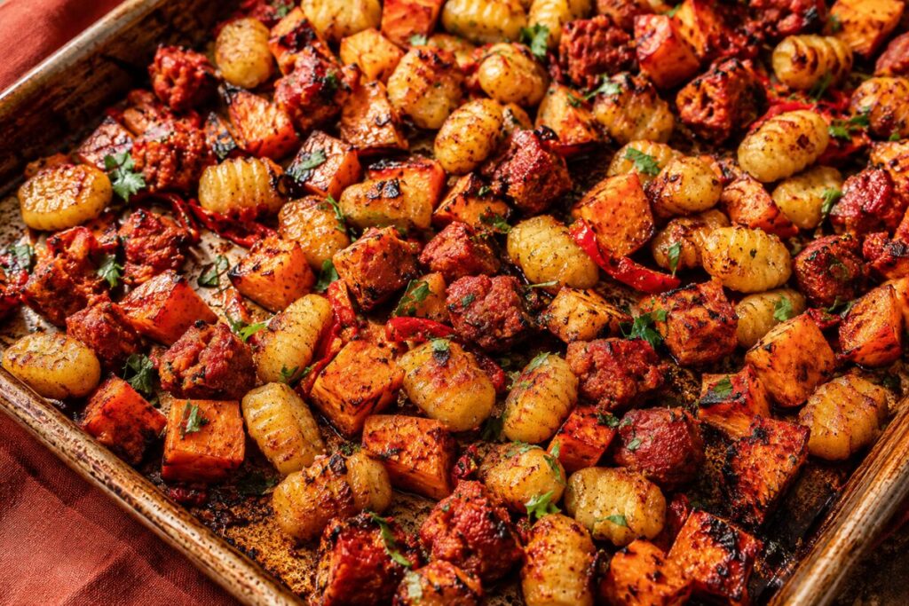 A spicy mix of chorizo, charred sweet potatoes, and roasted gnocchi on a baking sheet.