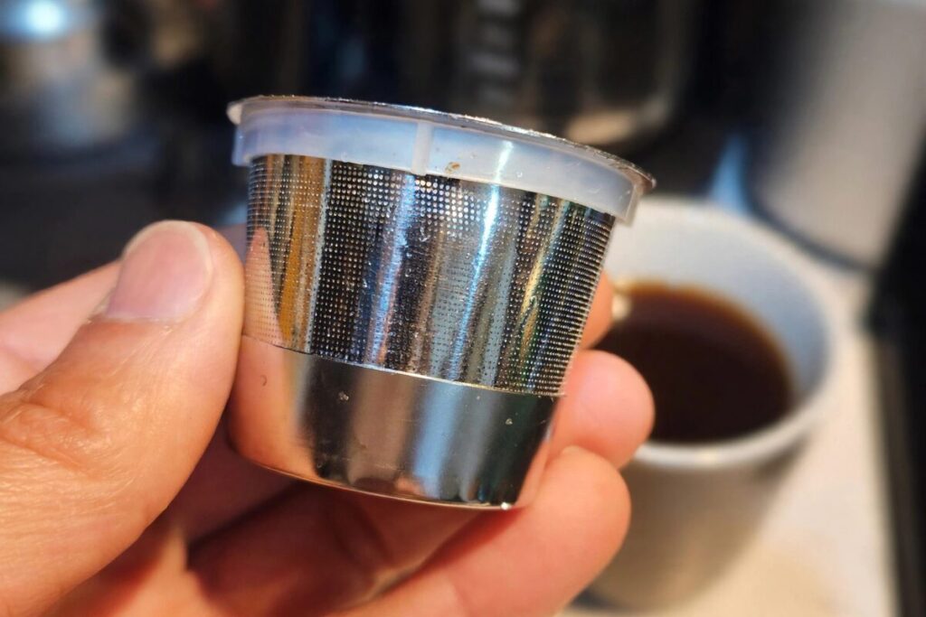 Fresh coffee and ground beans on a clean counter with a reusable coffee filter softly blurred behind them.